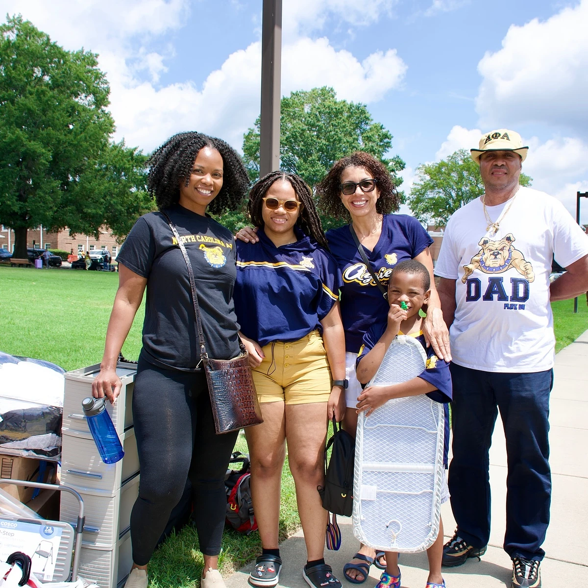 A family stands together outdoors, smiling and dressed in matching school spirit attire.